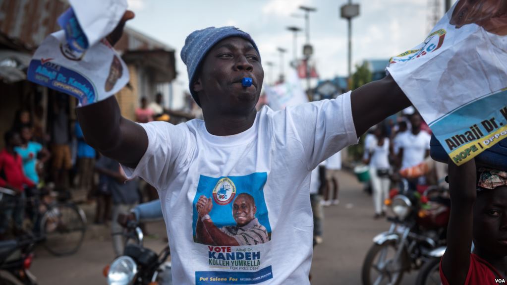 A supporter of the National Grand Coalition waves campaign posters during a rally in Bo, Sierra Leone, on March 4, 2018. (J. Patinkin/VOA)