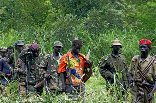 A group of armed men in military uniforms standing in a lush green jungle.