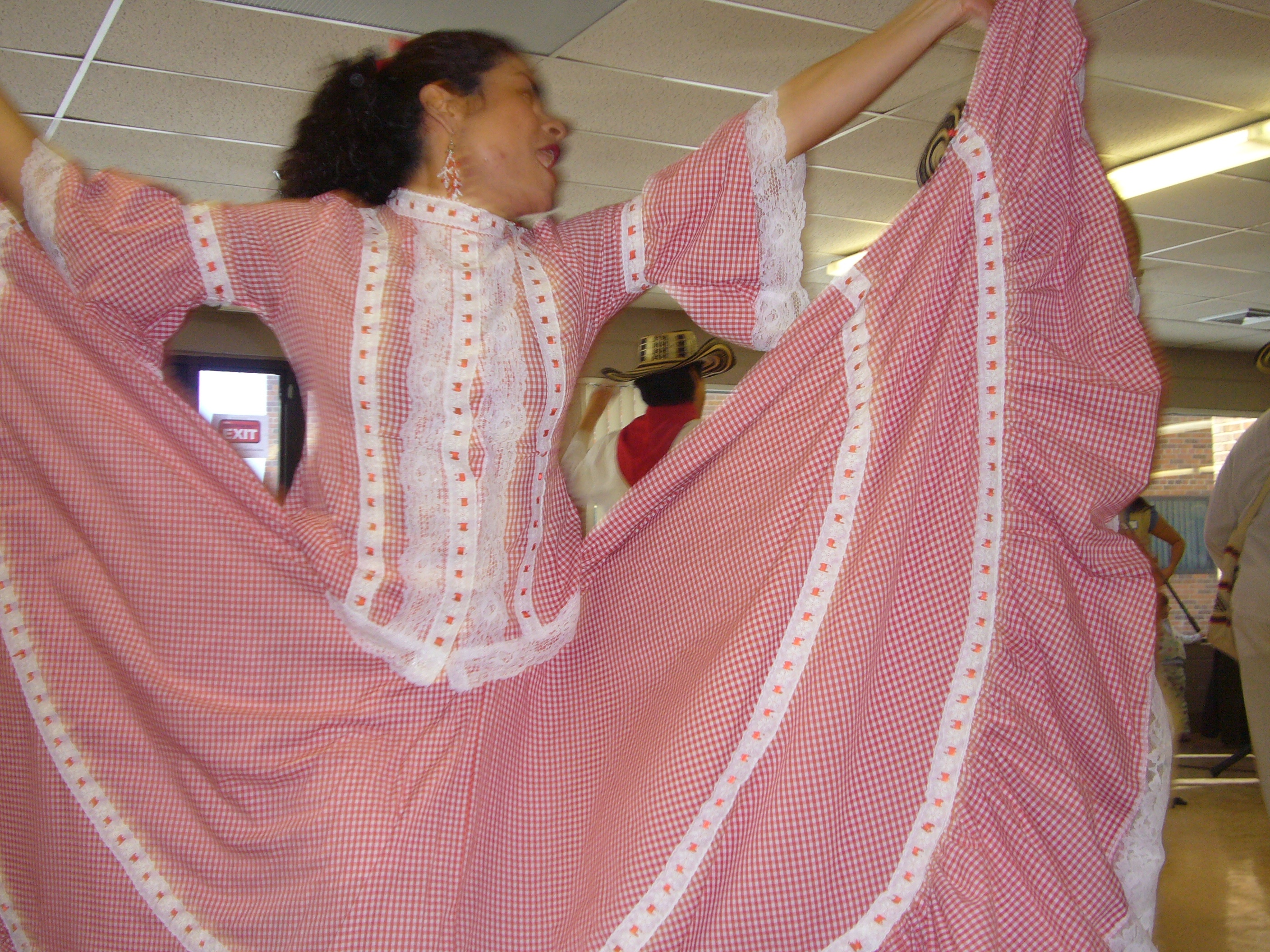 Woman in a pink folkloric dress dancing with a raised swirling skirt in a festive indoor environment.