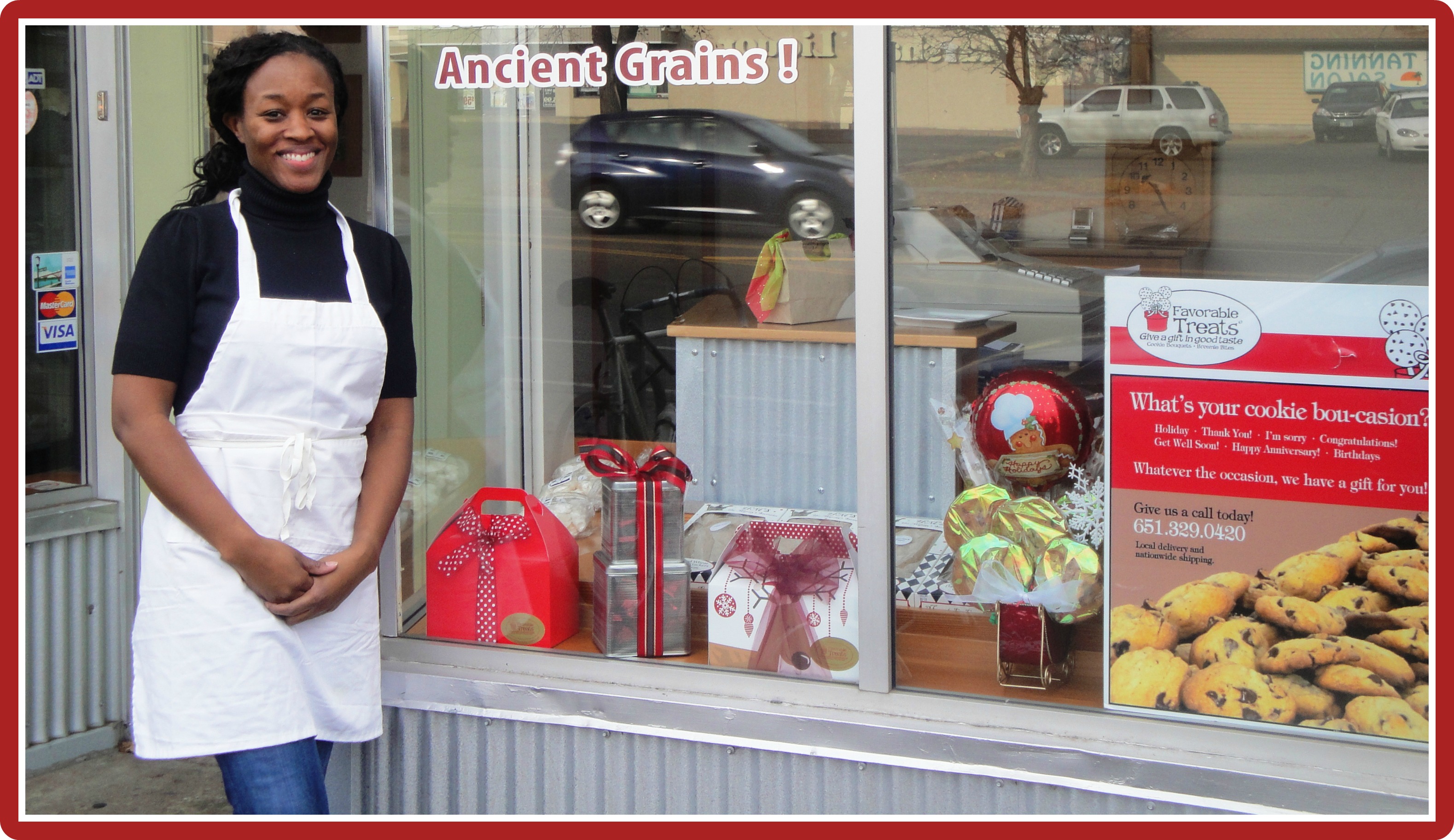 A woman in an apron smiles outside a bakery with a display window. signs and baked goods are visible, along with the text "ancient grains!" above her.