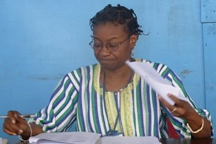 Middle-aged woman in glasses and striped top reviews documents at a blue table.