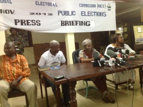 Four people seated at a table during a press briefing under a banner reading "electoral commission (nec) public elections nov. 2012.