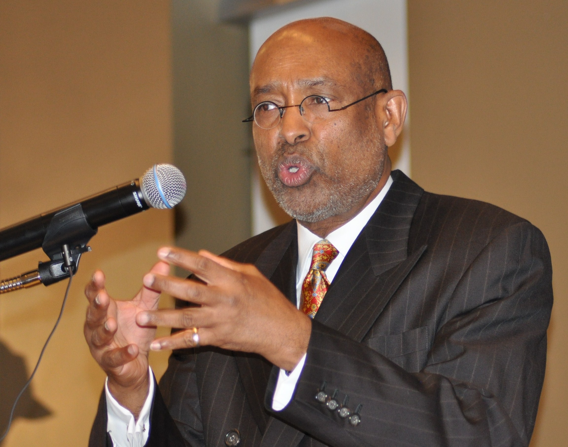 A man in a suit and tie speaking at a microphone.