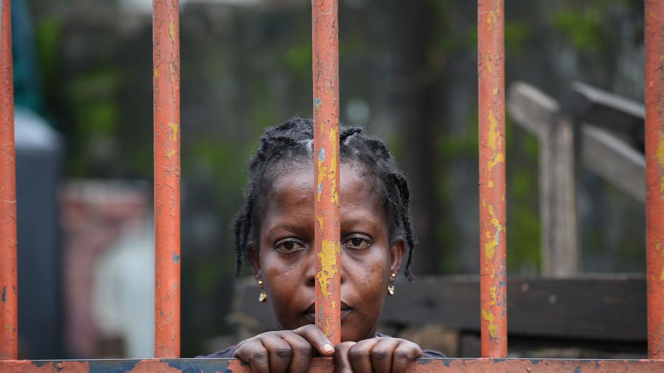 A woman with her hands on the bars of an orange fence.