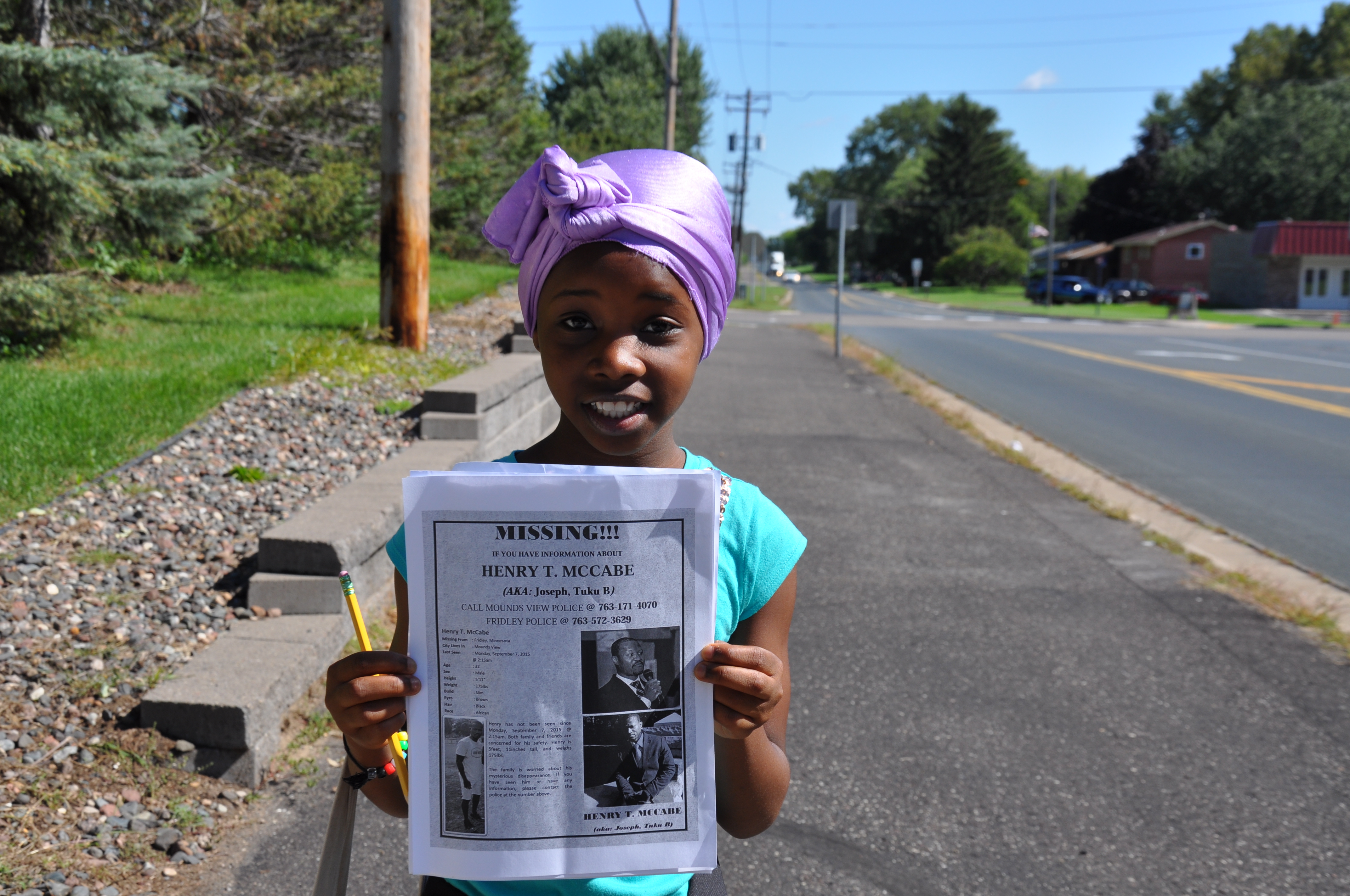 A girl holding up a newspaper on the side of the road.