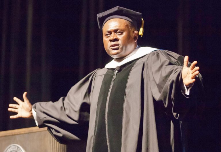 A man in graduation robes and cap standing on stage.