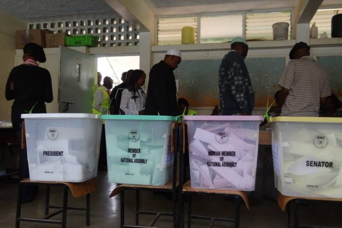 A group of people standing around some voting booths.