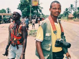 Two men are walking down the street with a camera.