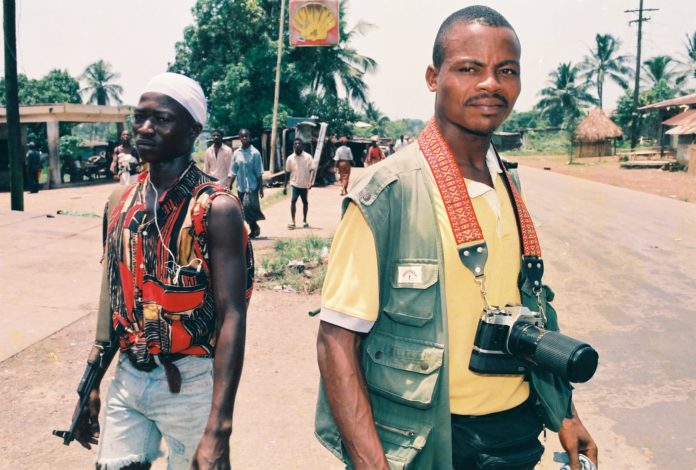 Two men are walking down the street with a camera.