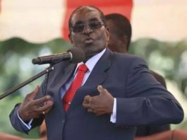 A man in a suit and red tie is speaking into a microphone.
