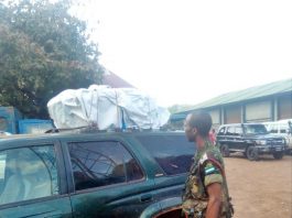 A soldier standing next to a car with a tarp on top.