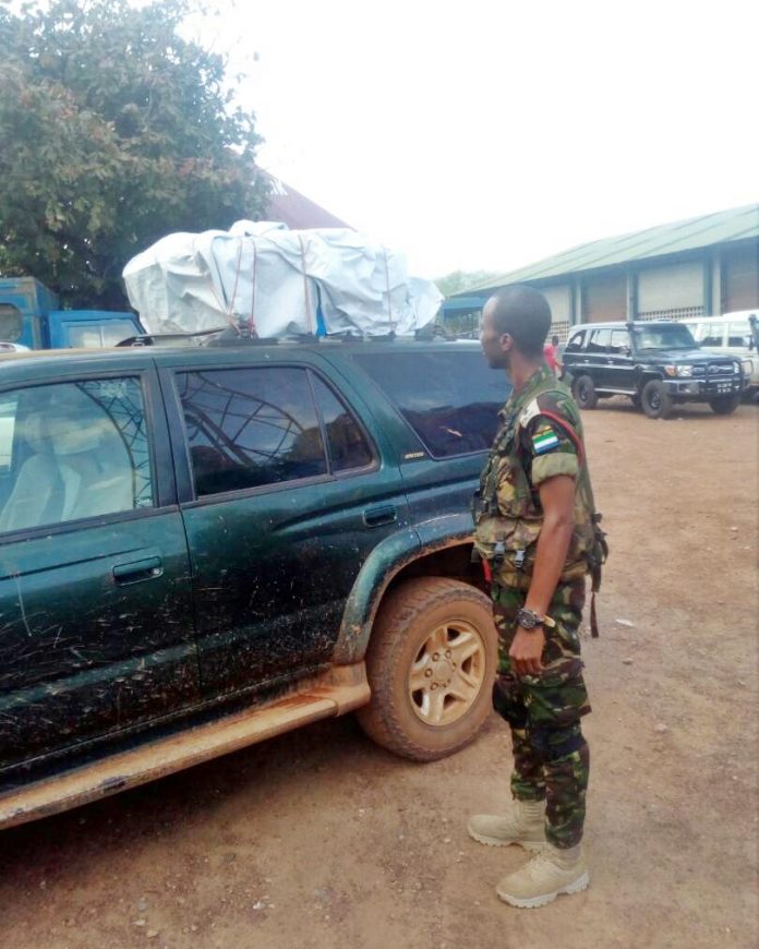 A soldier standing next to a car with a tarp on top.