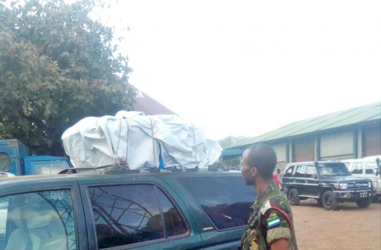 A soldier standing next to a car with a tarp on top.