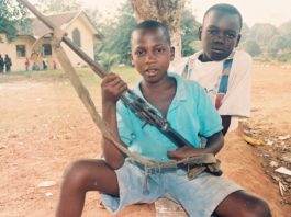 Two boys holding guns and a bow in their hands.