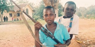 Two boys holding guns and a bow in their hands.
