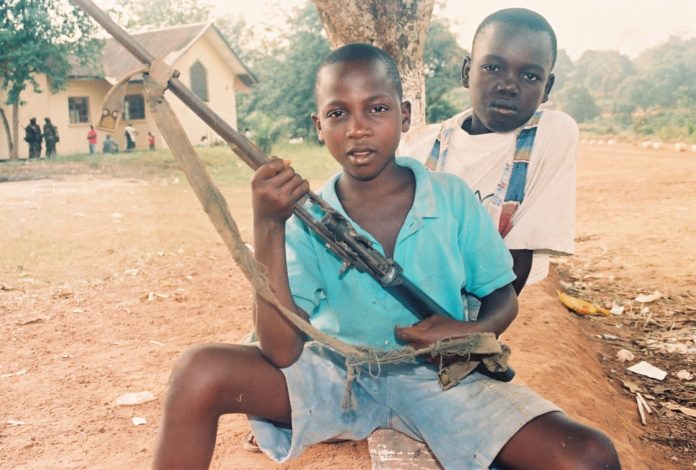 Two boys holding guns and a bow in their hands.