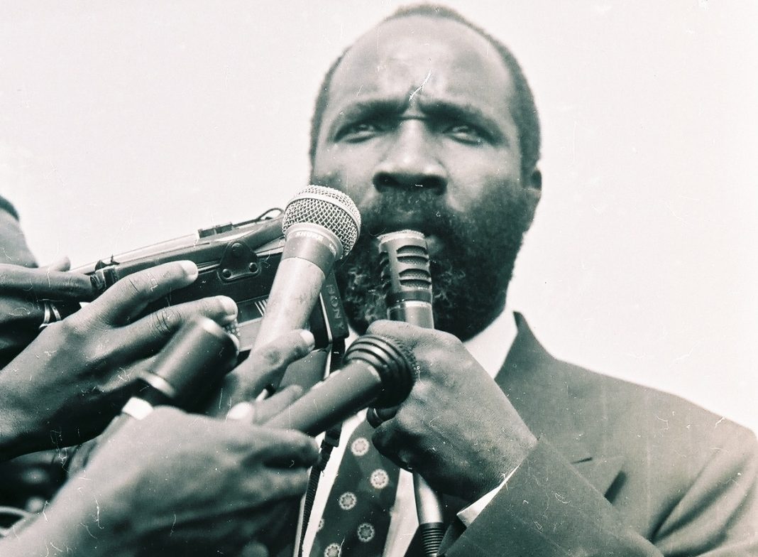 A man in suit and tie holding up several microphones.