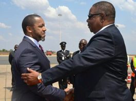 Two men in suits shaking hands near a police officer.