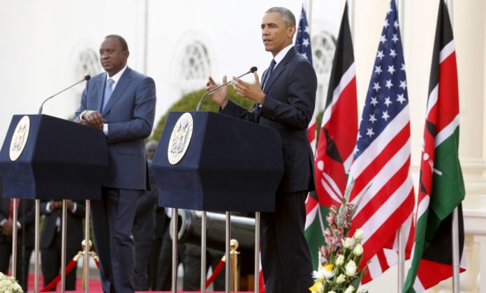 President obama speaking at a podium in front of flags.