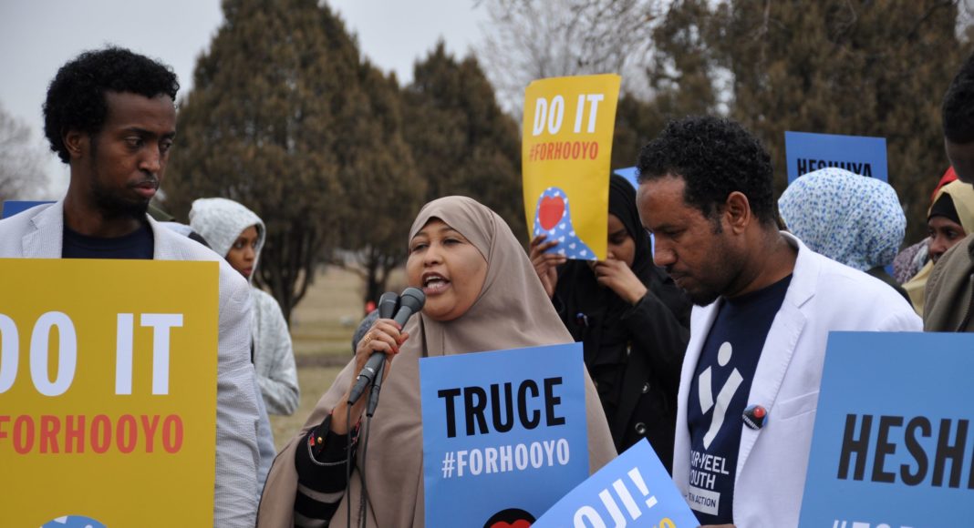 A woman speaking at an event with other people holding signs.