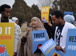 A woman speaking at an event with other people holding signs.