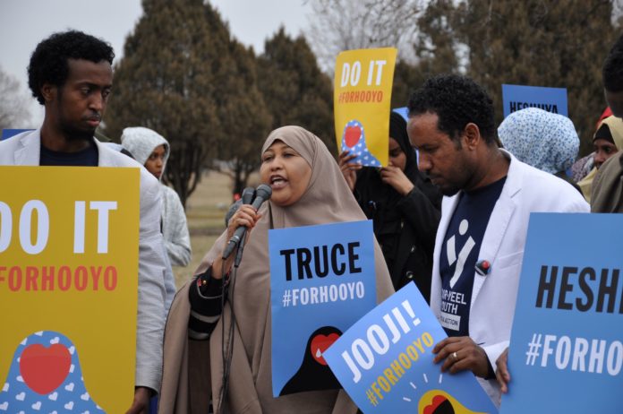 A woman speaking at an event with other people holding signs.