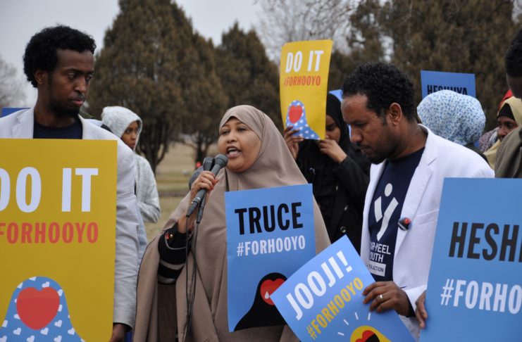 A woman speaking at an event with other people holding signs.